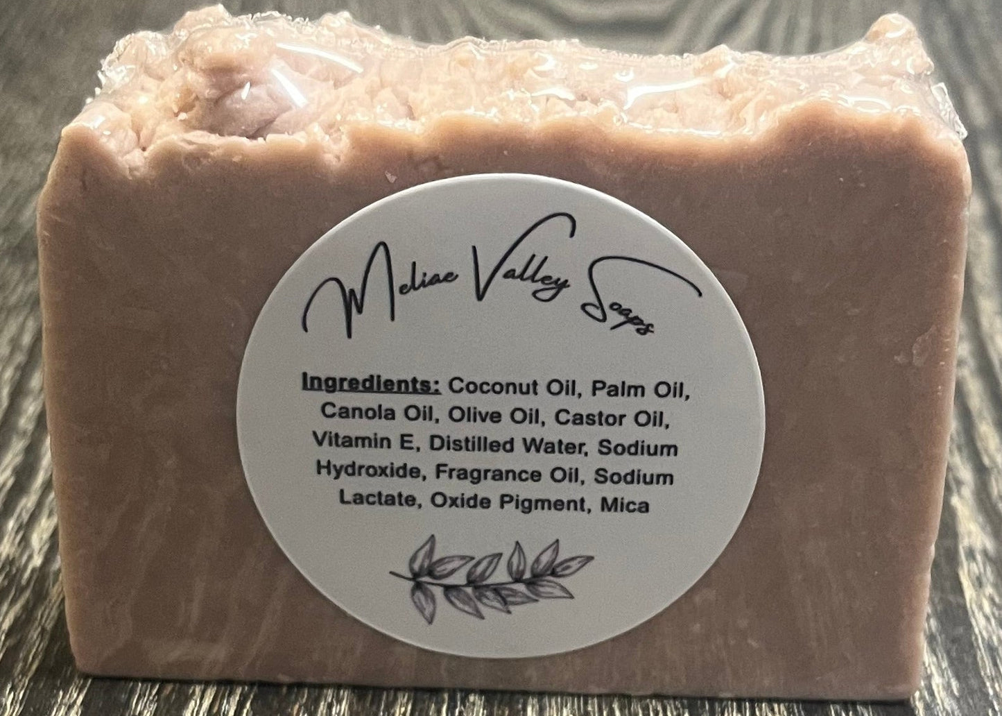 A light purple bar of soap with a white label with the ingredients on a dark wooden surface.