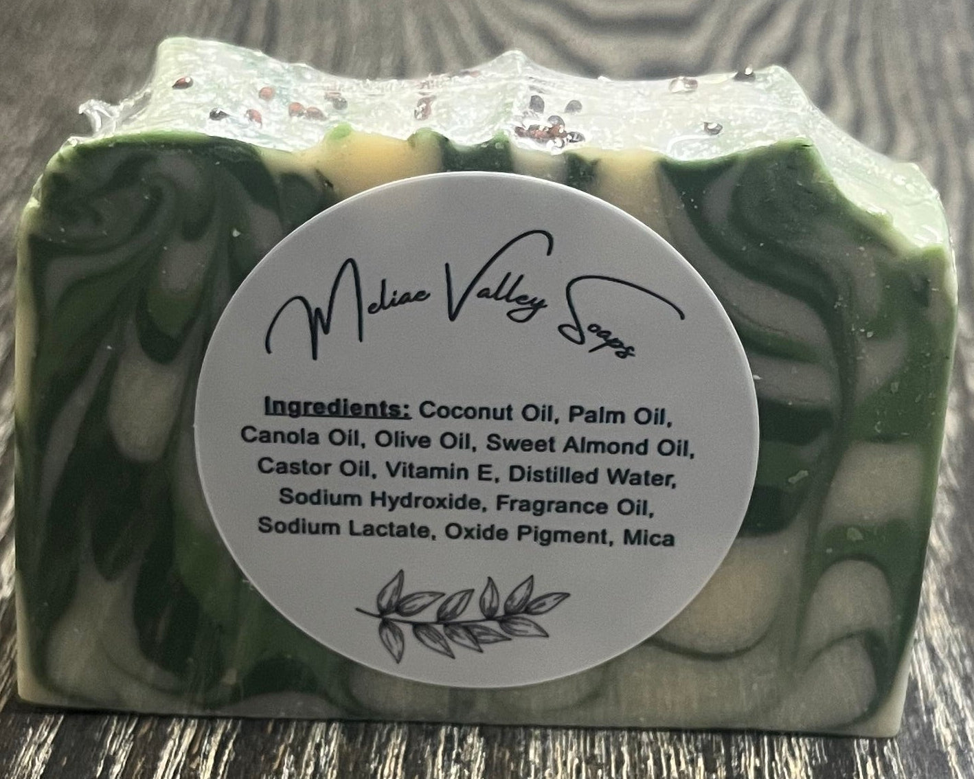 Green and white marbled soap with a white label with the ingredients on a wooden surface.