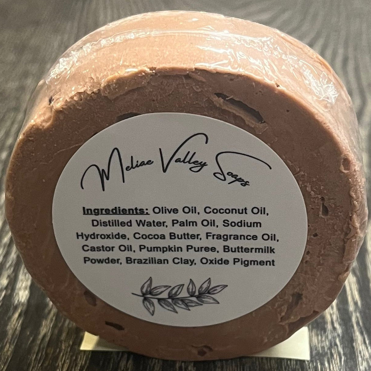 Round brown soap bar with a white label with the ingredients on a wooden surface.
