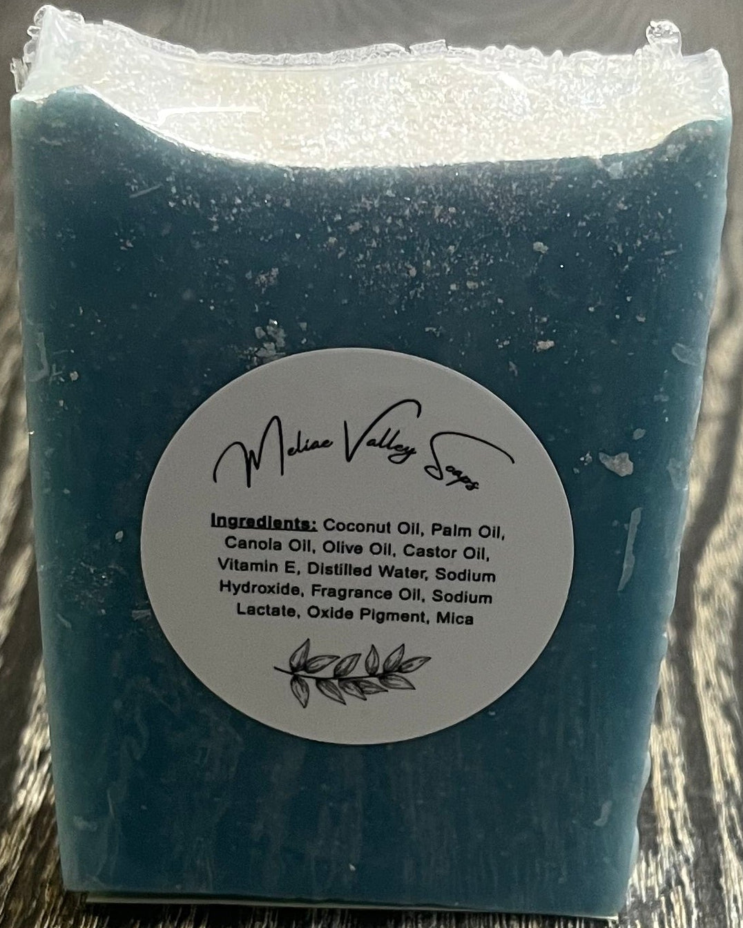 A tall blue bar of soap with a heavy sprinkle of glitter on top faces the camera, showing a label with the ingredients.