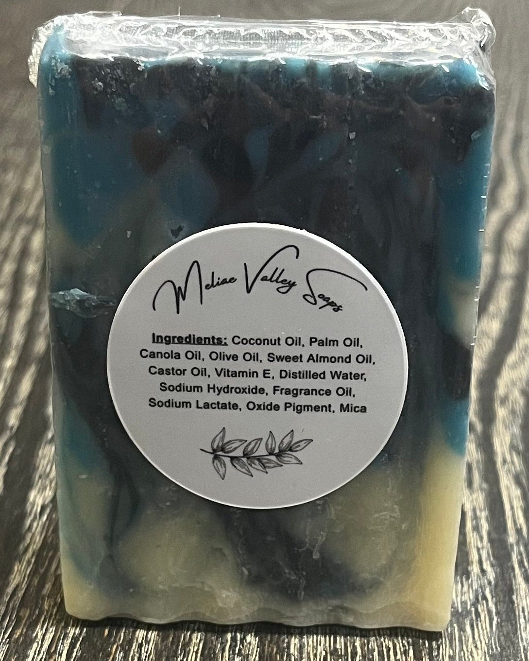 Bar of soap with navy blue, blue, and white swirl design with a white label with the ingredients on it on a wooden surface.
