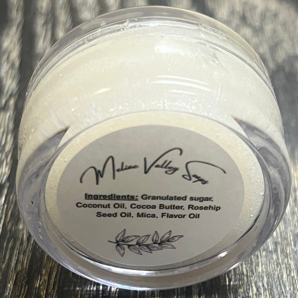 A lip pot filled with sugar dyed white. The lip pot is positioned on its side with its ingredients label facing the camera.