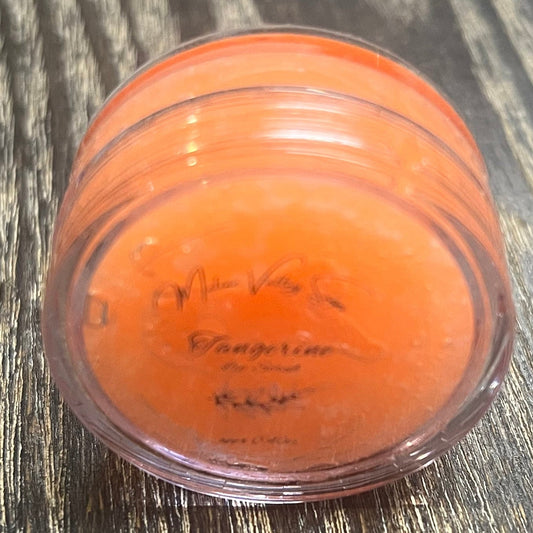 A lip pot filled with sugar dyed orange. The lip pot is positioned on its side with its label facing the camera.