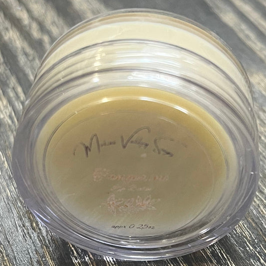 A lip pot filled with lip balm. The lip pot is positioned on its side with its label facing the camera.