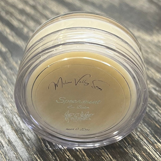 A lip pot filled with lip balm. The lip pot is positioned on its side with its label facing the camera.