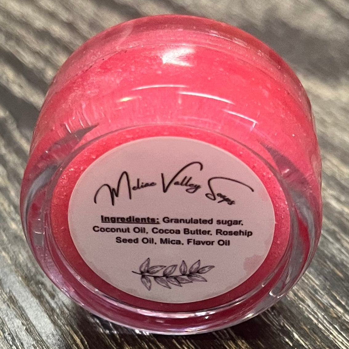 A lip pot filled with sugar dyed red. The lip pot is positioned on its side with its ingredients label facing the camera.