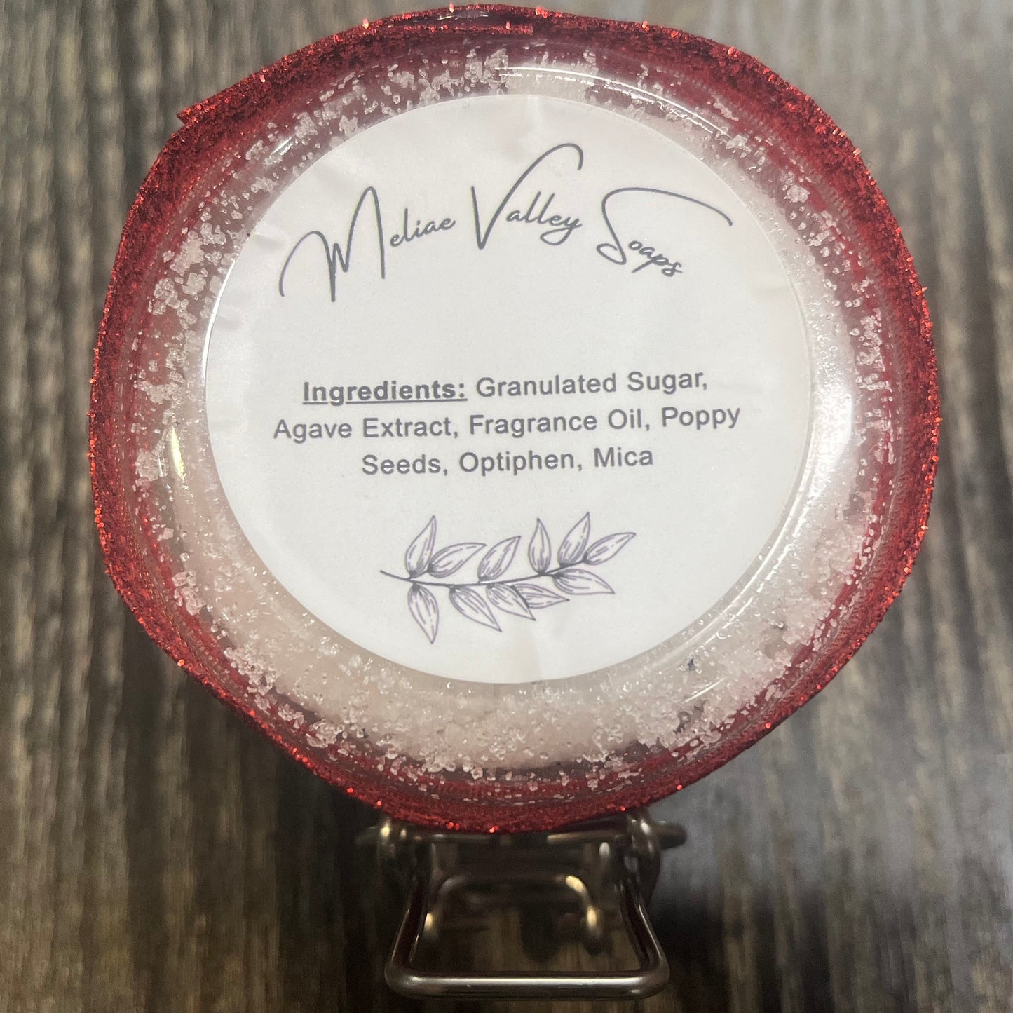 The bottom of a jar with a red ribbon around it. The bottom of the jar has a white sticker with the ingredients on it.