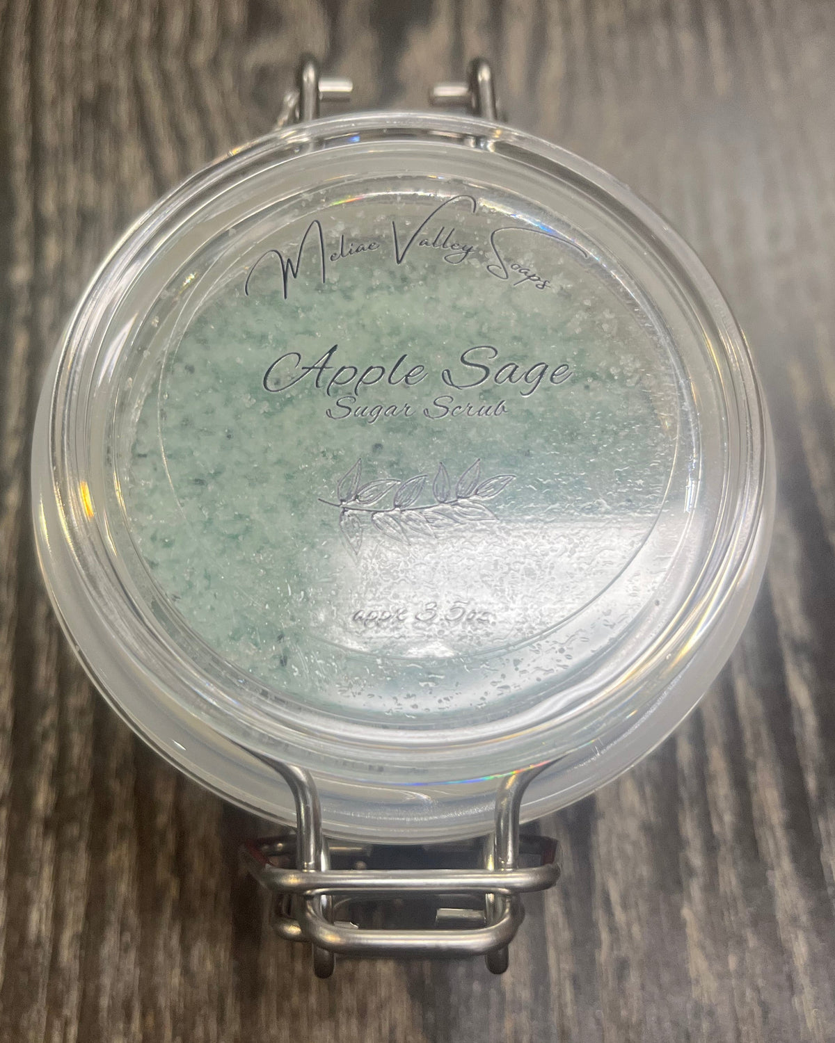 Clear round jar with a sticker on top. You see through the jar to green sugar.