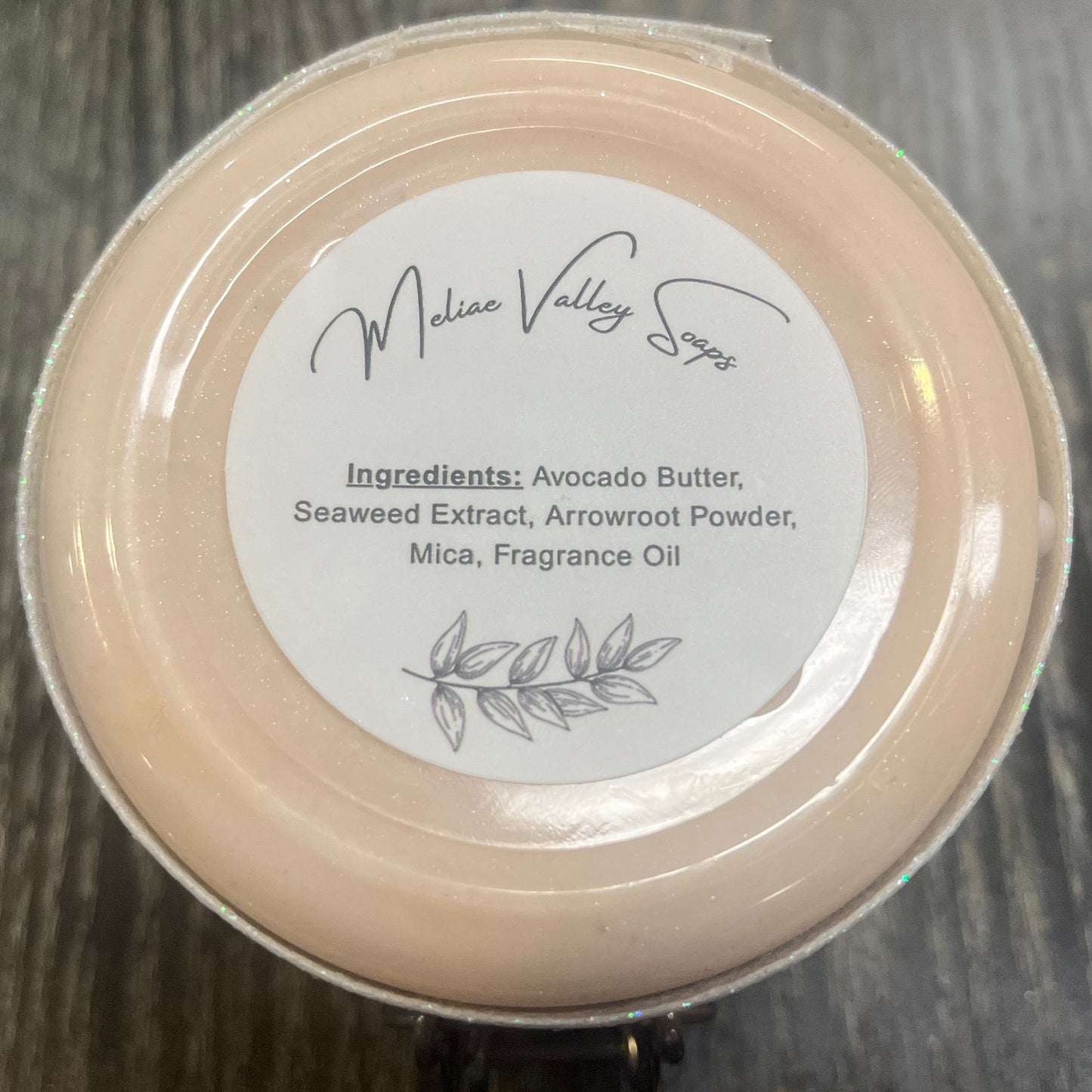 The bottom of a jar with a white ribbon around it. The bottom of the jar has a white sticker with the ingredients on it.