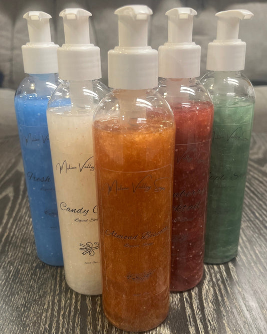 A set of pump bottles with different colored liquids, bronze, white, blue, red, and green, in a 'V' shape on a wooden surface.