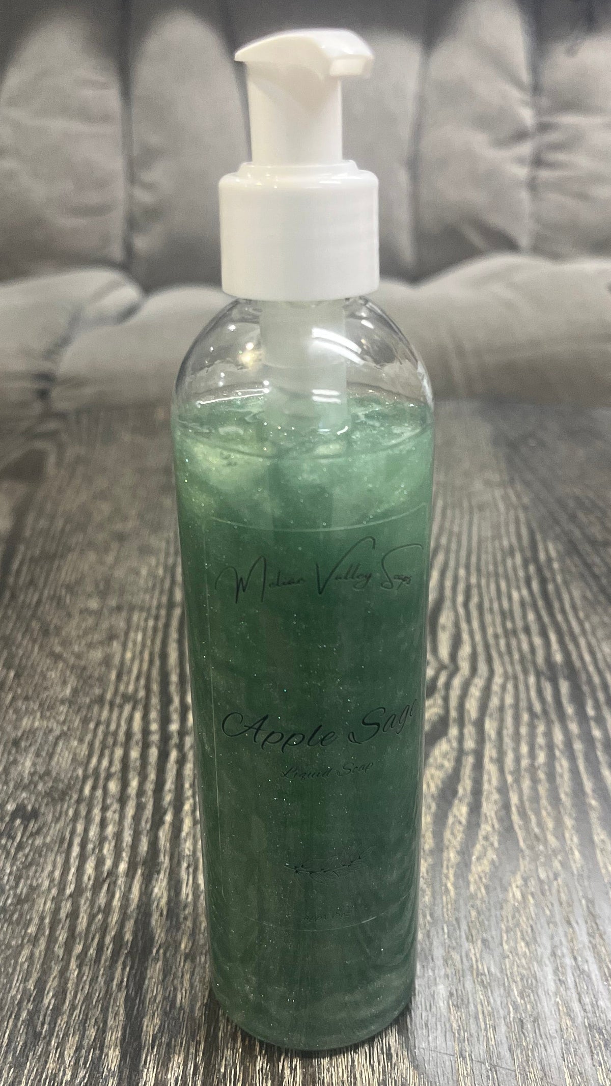 A clear pump bottle with a white nozzle full of green liquid on a textured surface.