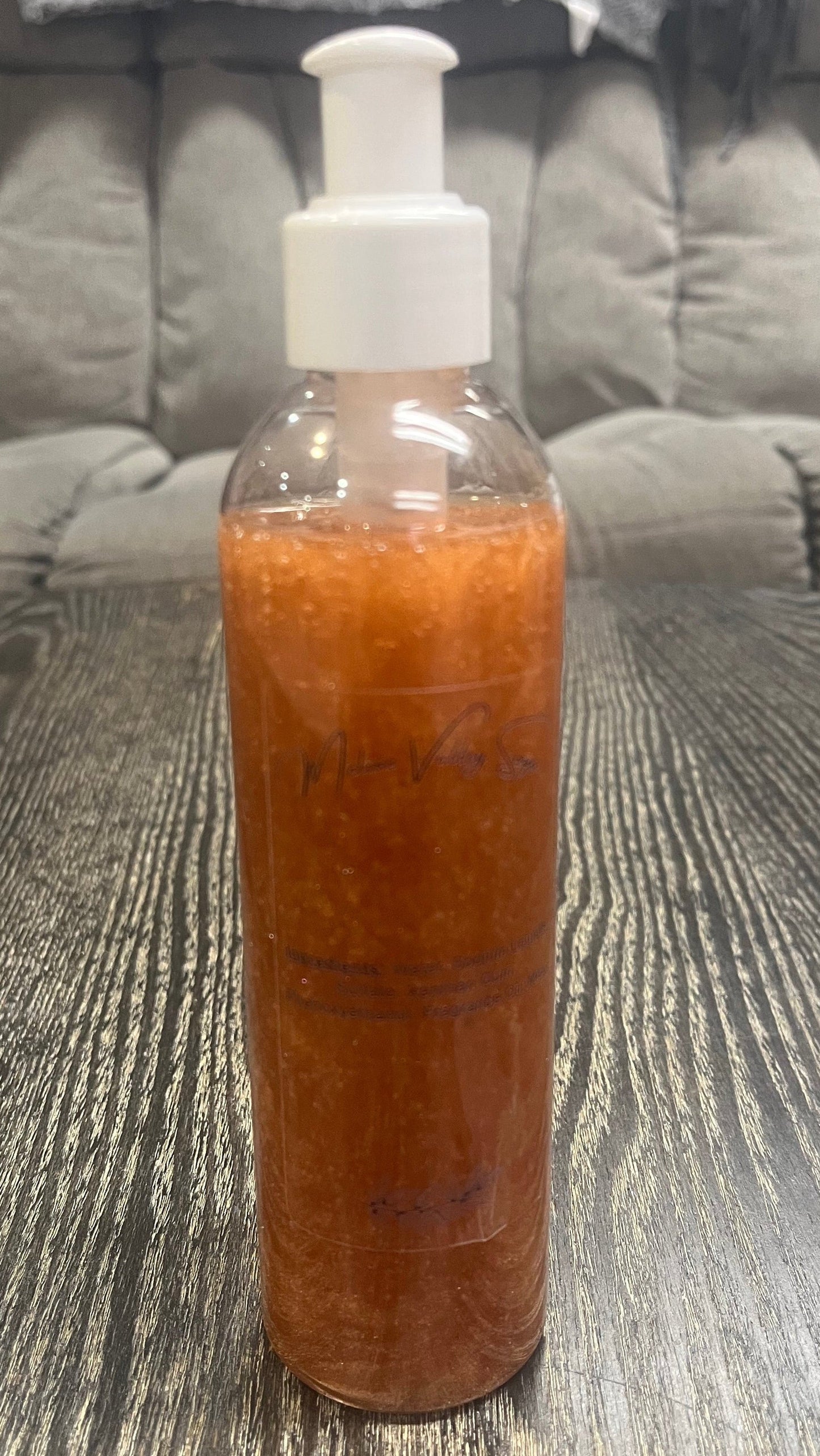 A clear pump bottle with a white nozzle full of bronze liquid on a textured surface.