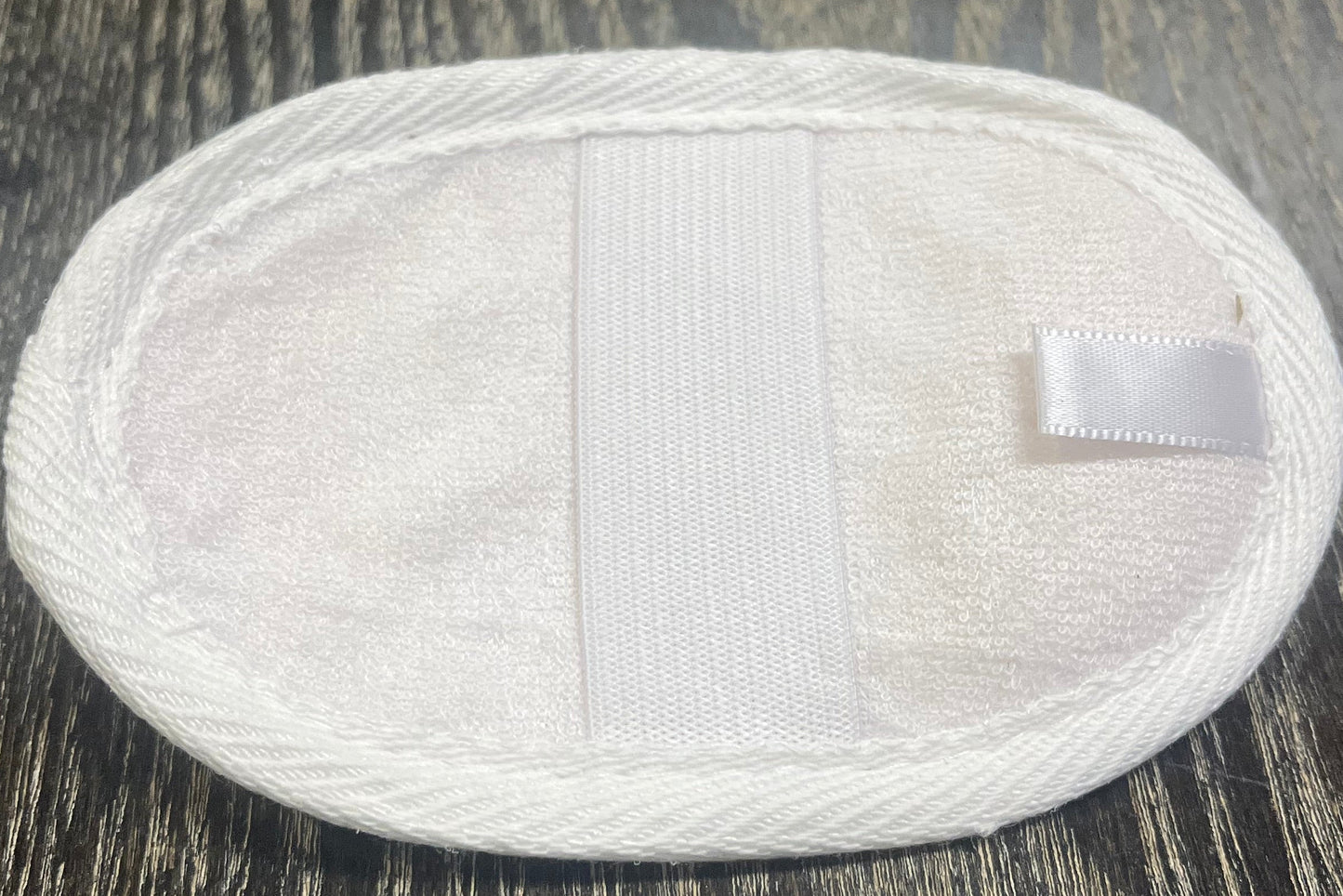 Round, white, loofah pad with an elastic band on a dark wooden surface.