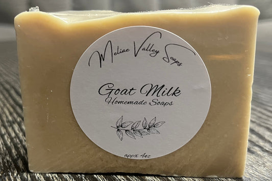 A beige bar of goat milk soap with a label on a wooden surface.