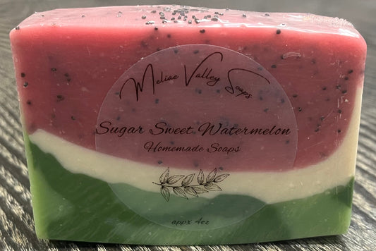 A bar of pink, white, and green soap with a label on a wooden surface.