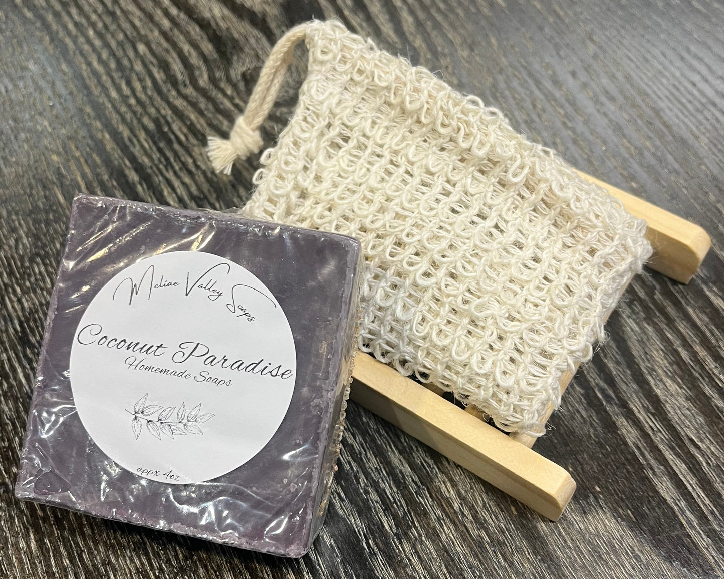 A purple bar of soap with a wooden stand and an exfoliating bag on a dark wooden surface.