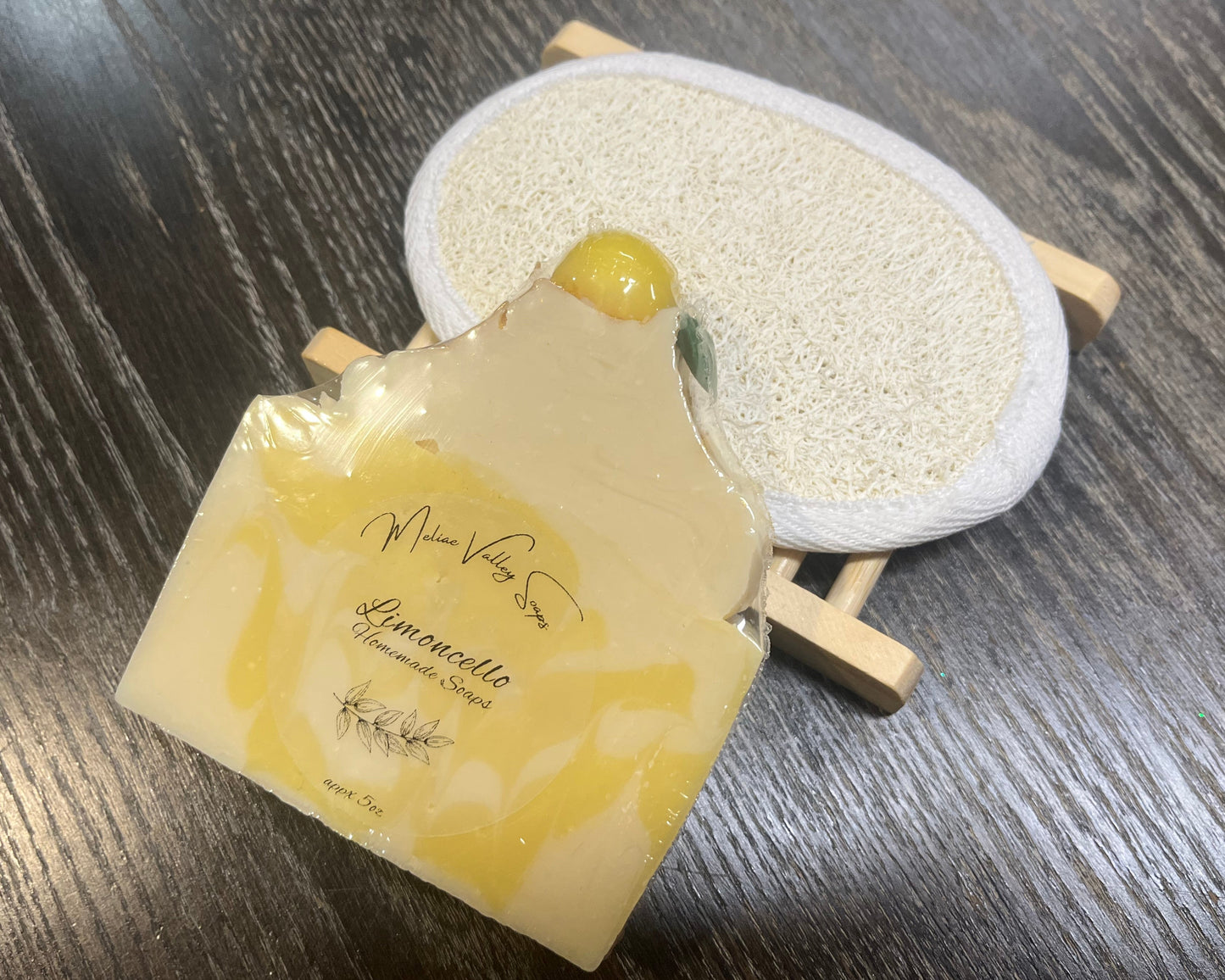A yellow and white soap bar with a wooden stand and a loofah pad on a dark wooden surface.