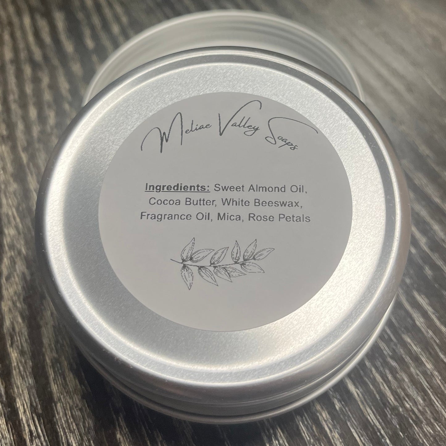 An round metal tin showing with a white ingredients label on a dark wood-grain surface.