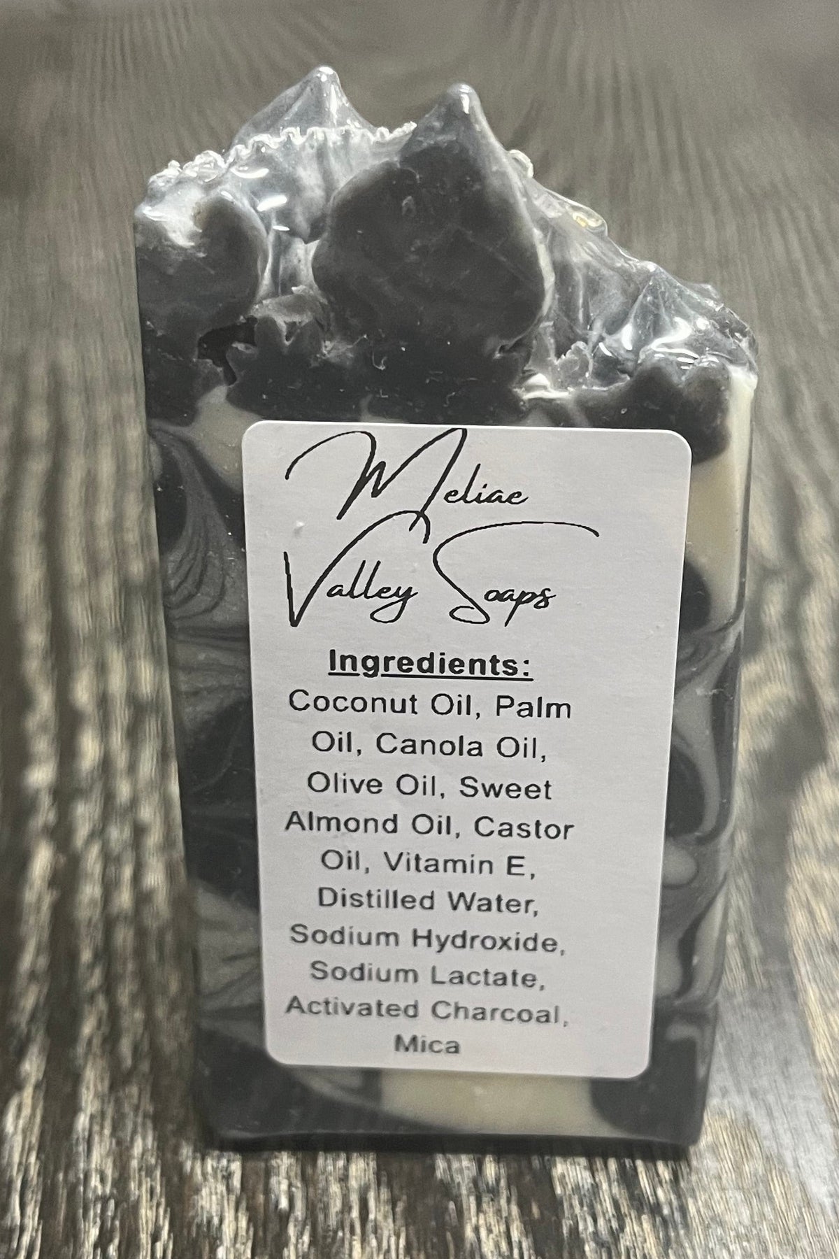 A handmade soap bar with black and white marbled swirls and a pointed top. It has a white ingredients label.