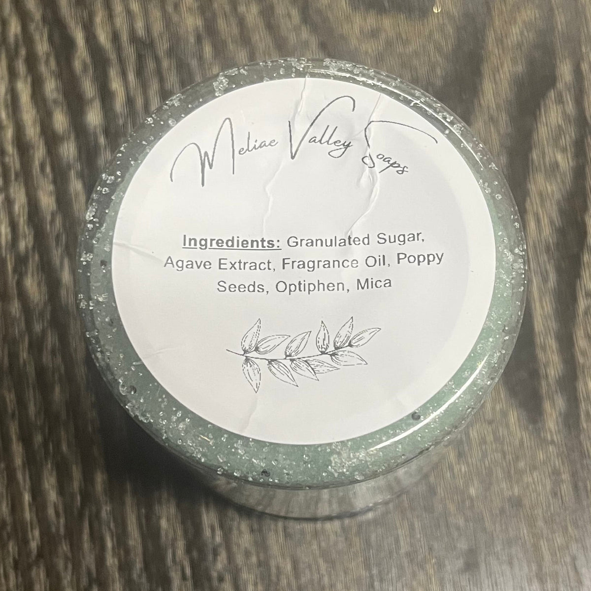 Jar of green sugar body scrub with a white ingredients label.