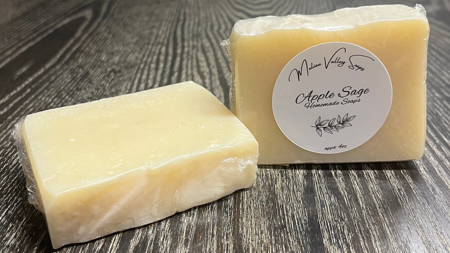 Two bars of uncolored soap on a wooden surface. The left one is face down, showing the plain back and top. The right one is upright, showing the front with a white label. 