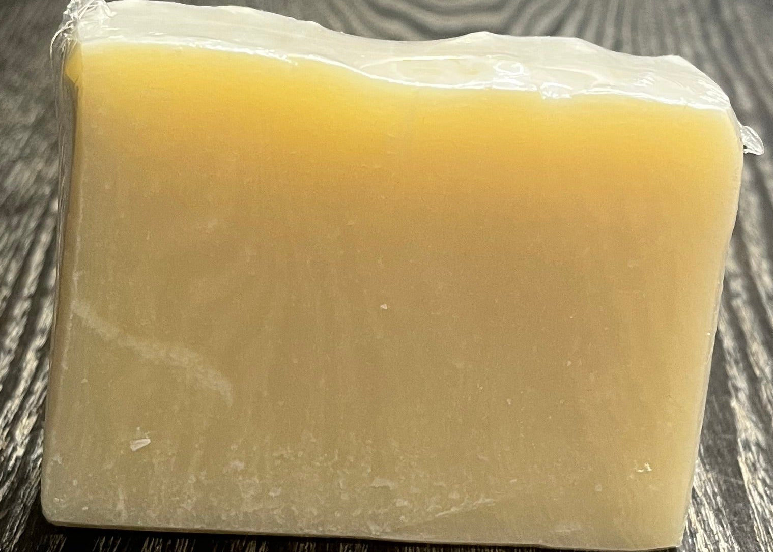 Block of uncolored soap on a wooden surface with a blurred background.