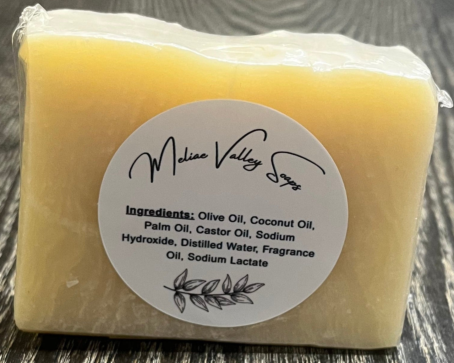 Bar of uncolored soap on a wooden surface with a white label with ingredients.