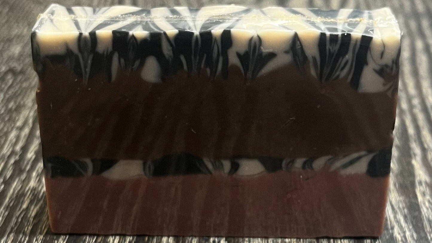 A bar of soap with four layers. The bottom layer is solid pink, the third layer is black and white marble, the second layer is solid brown, and the top layer is also black and white marble. 