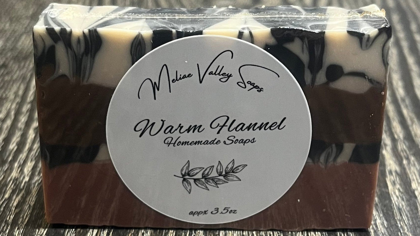 A bar of soap with a white label showing it has four layers. The bottom layer is solid pink, the third layer is black and white marble, the second layer is solid brown, and the top layer is also black and white marble. 