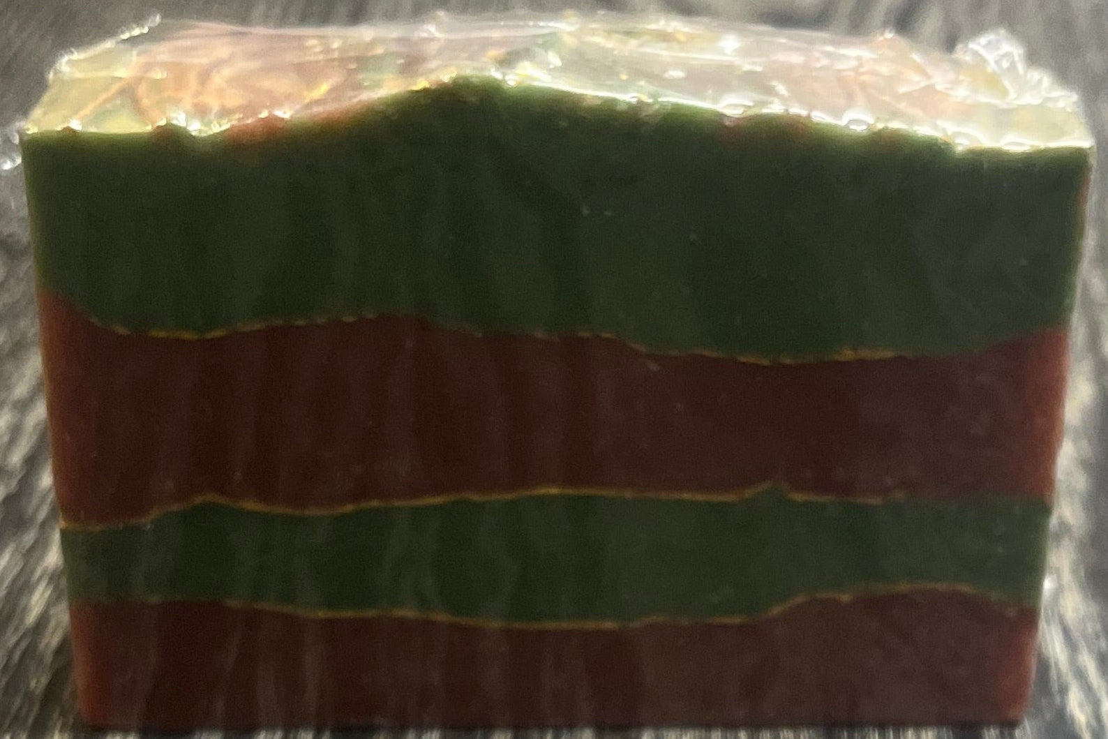 Bar of soap with green and red stripes with gold lines between the stripes on a wooden surface. 