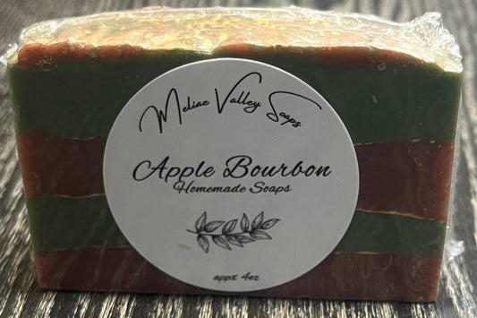 Block of soap with green and red stripes with gold lines between the stripes, with a white label on a wooden surface. 