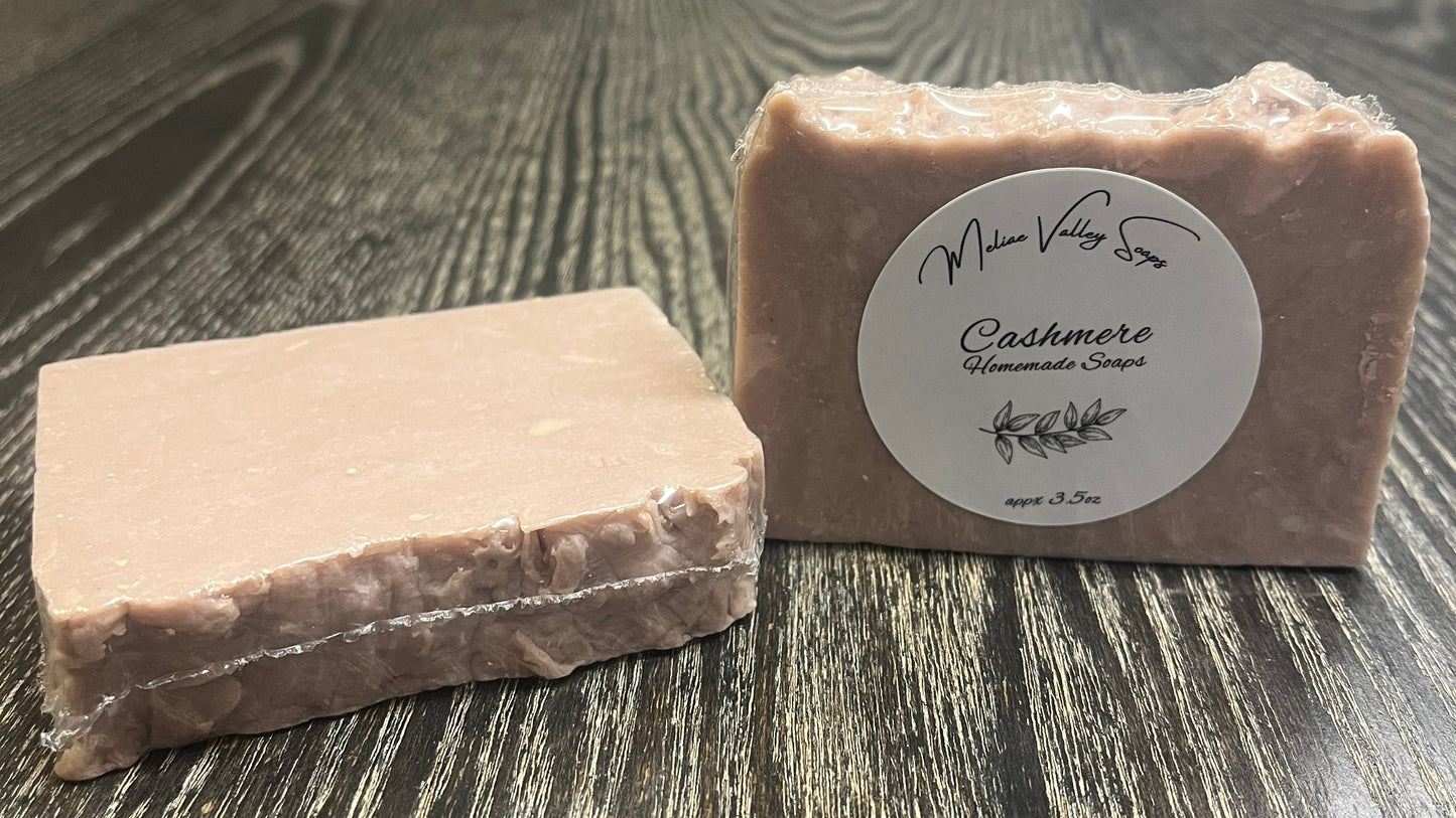 Two light purple bars of soap on a dark wooden surface. The left one is face down, while the right one is upright, showing a white label. 