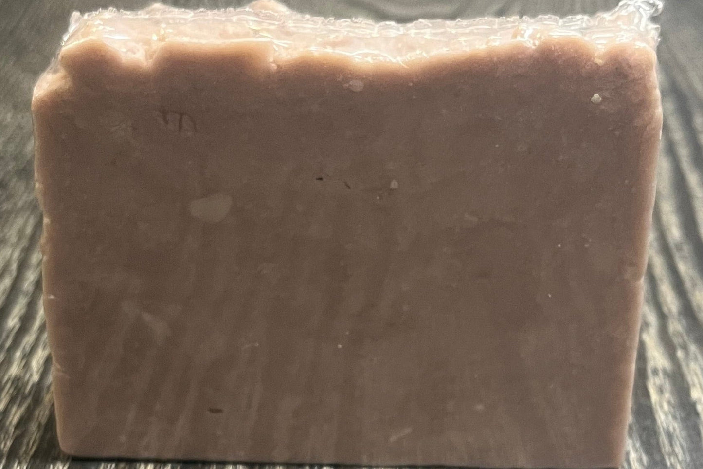 A light purple bar of soap on a dark wooden surface. 