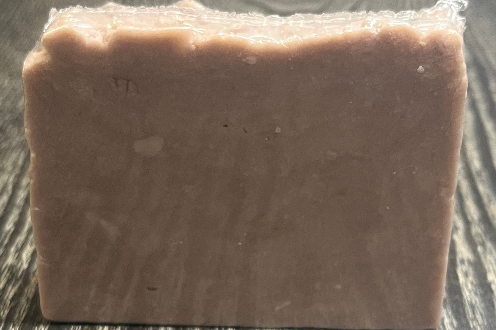 A light purple bar of soap on a dark wooden surface. 