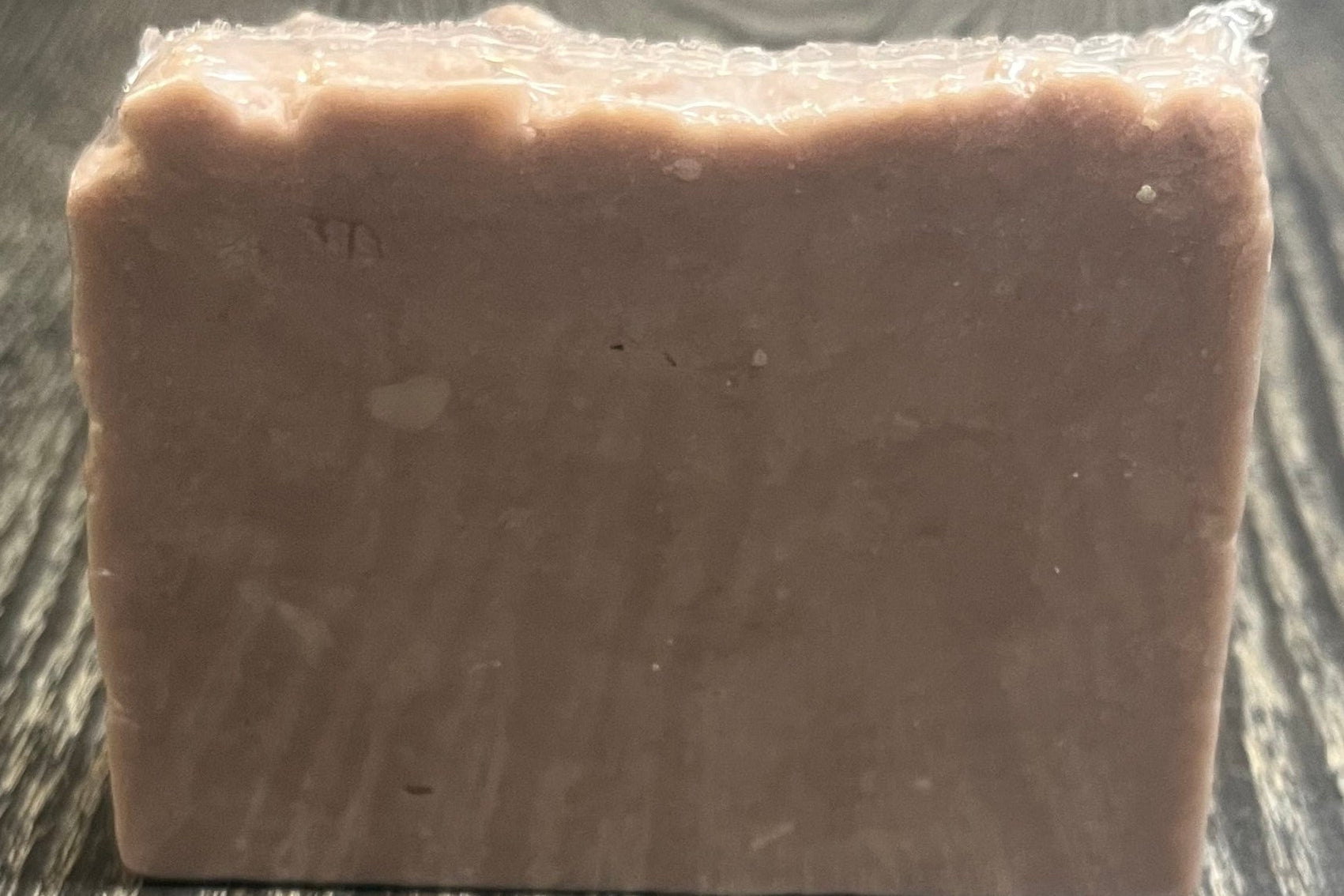 A light purple bar of soap on a dark wooden surface. 