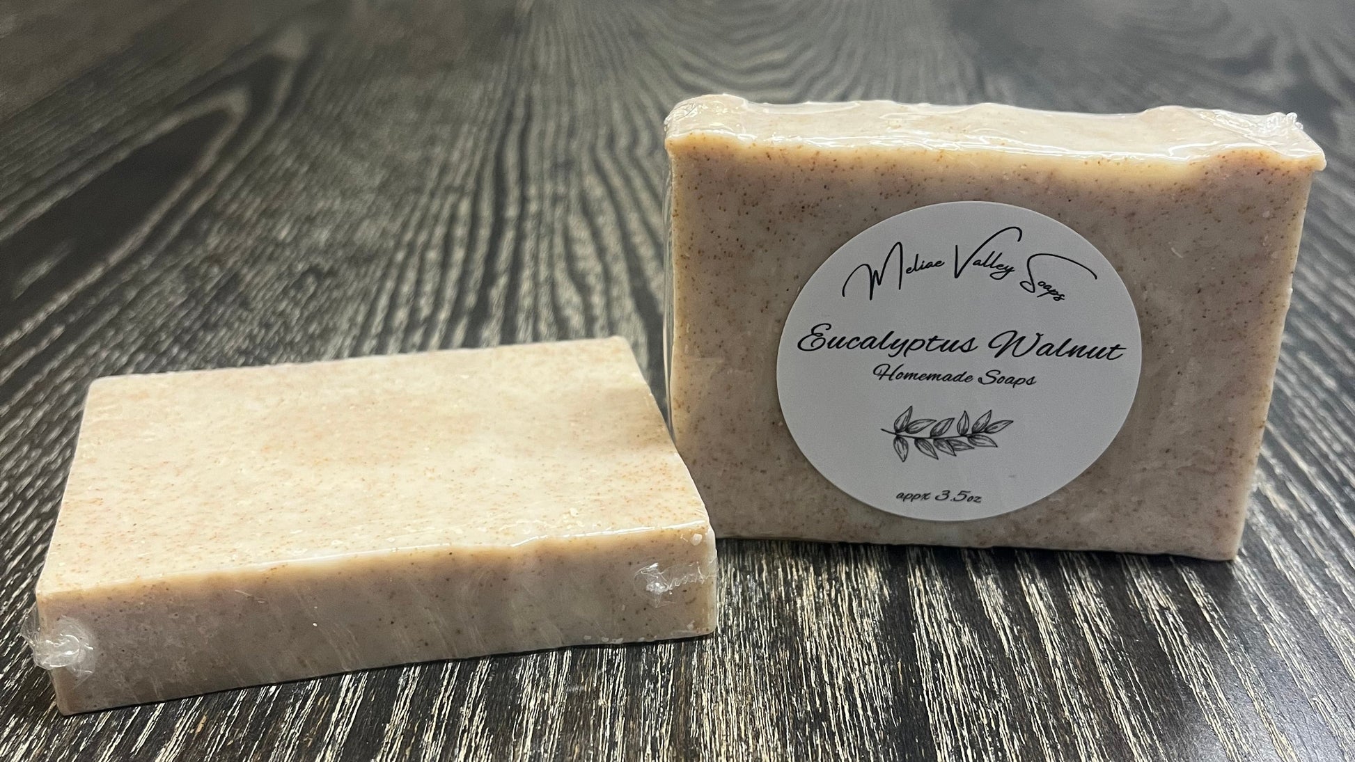 Two soap bars on a wooden surface with a label on one of them.