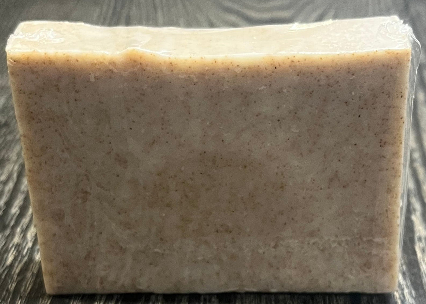 A beige soap bar with darker brown specs of ground walnut shells. 