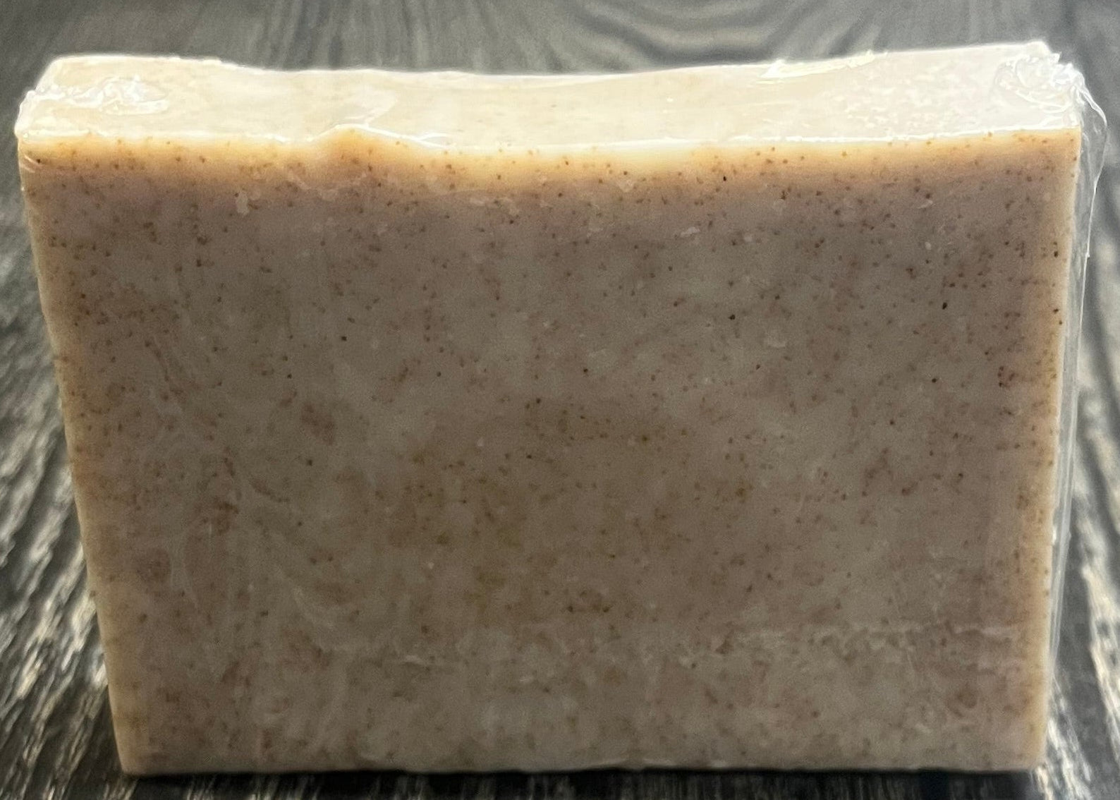 A beige soap bar with darker brown specs of ground walnut shells. 