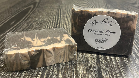 Two black and beige marble-patterned soap bars on a wooden surface. The left one is face down, showing the back and top. The right one is upright, showing the front of the bar with a label on it. 