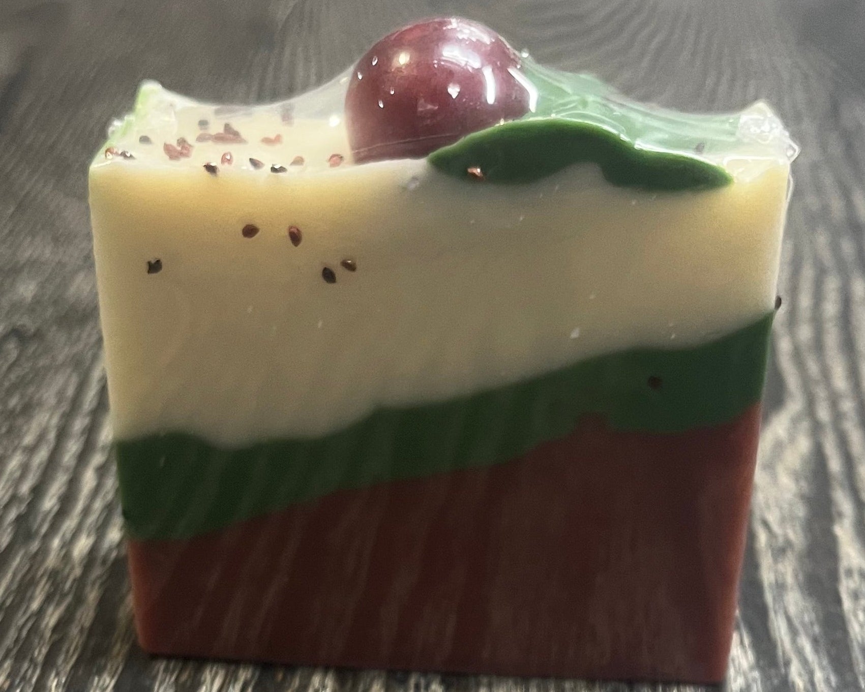 A bar of soap with three diagonal layers. The bottom layer is red, the middle layer is green, and a top white layer. On top of the bar there is a green leaf coming from a red sphere. 