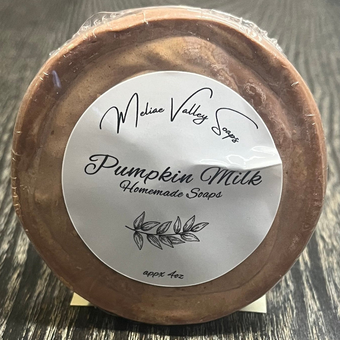 Round brown soap bar with a white label on a wooden surface. 