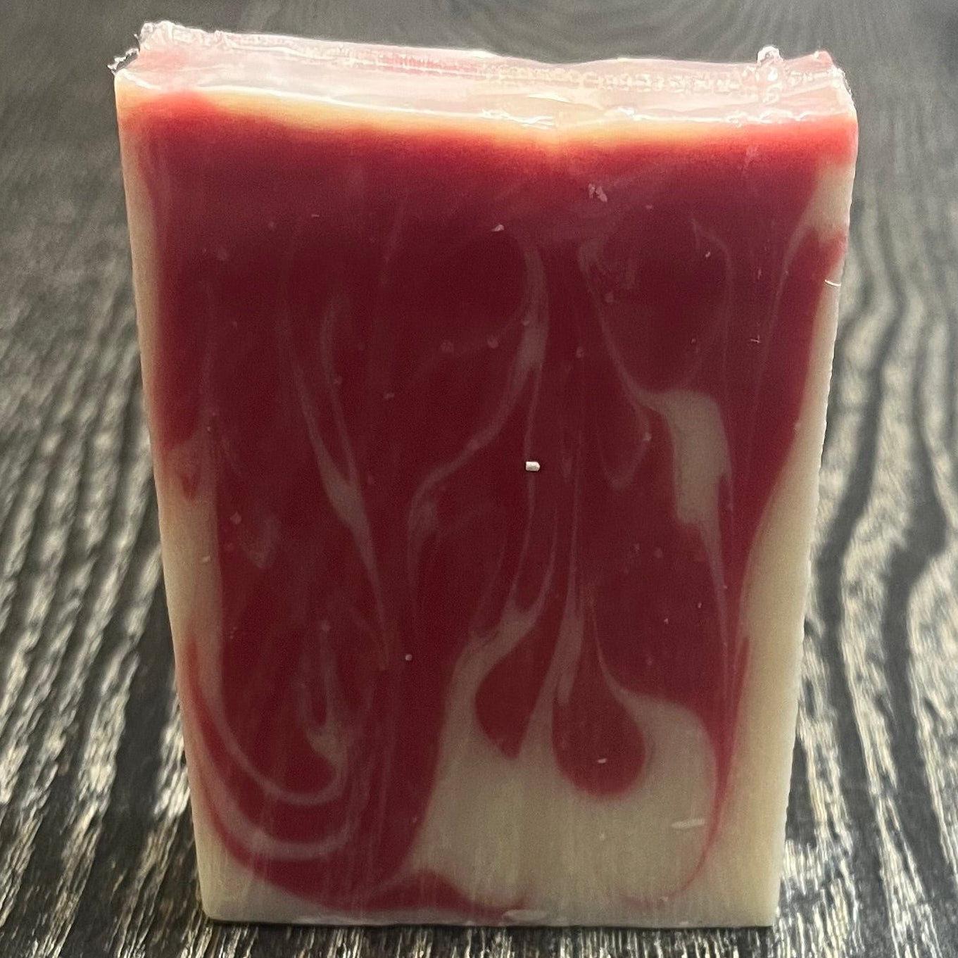 A bar of red and white marbled soap on a dark wooden surface.