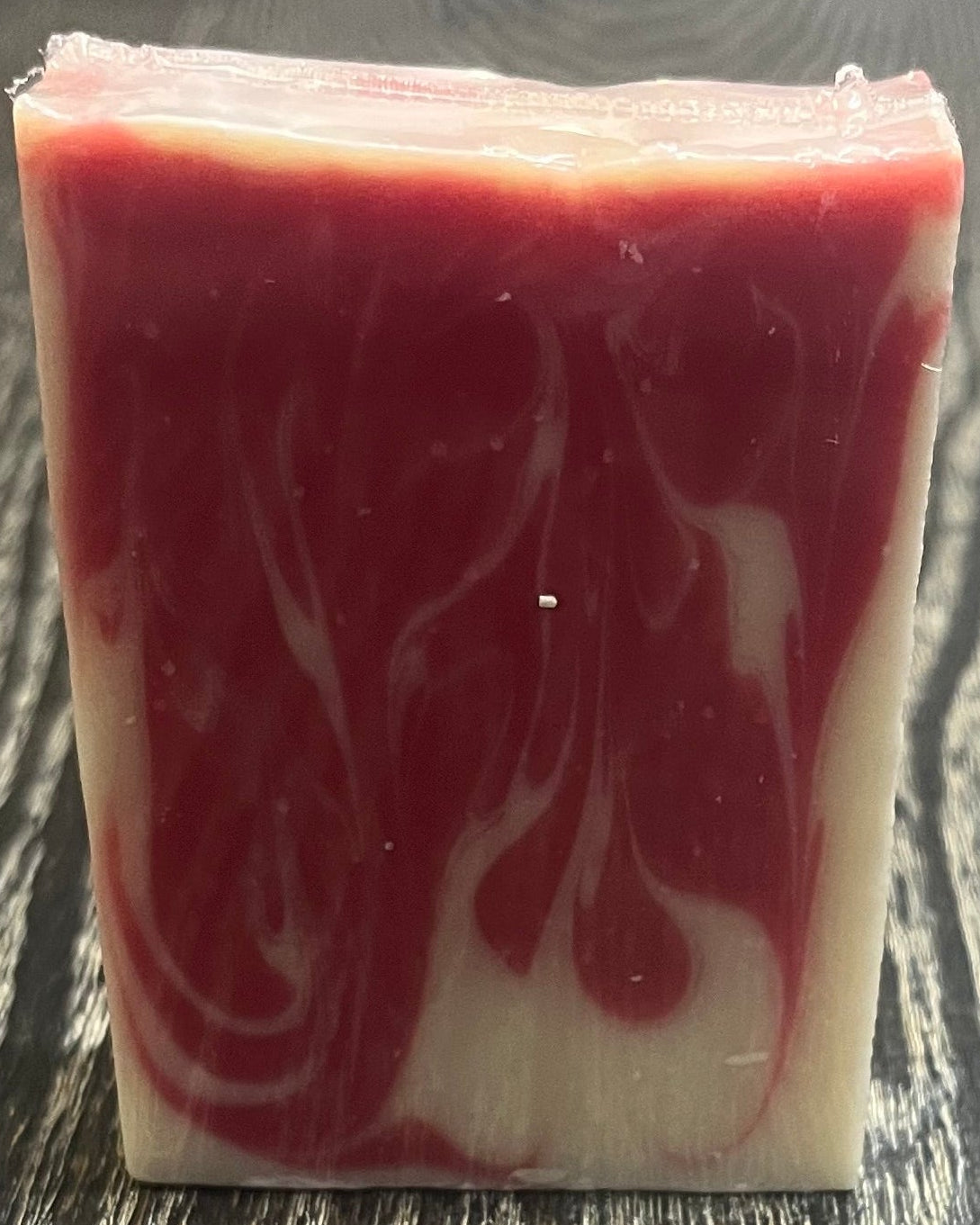 Block of red and white marbled soap on a dark wooden surface.