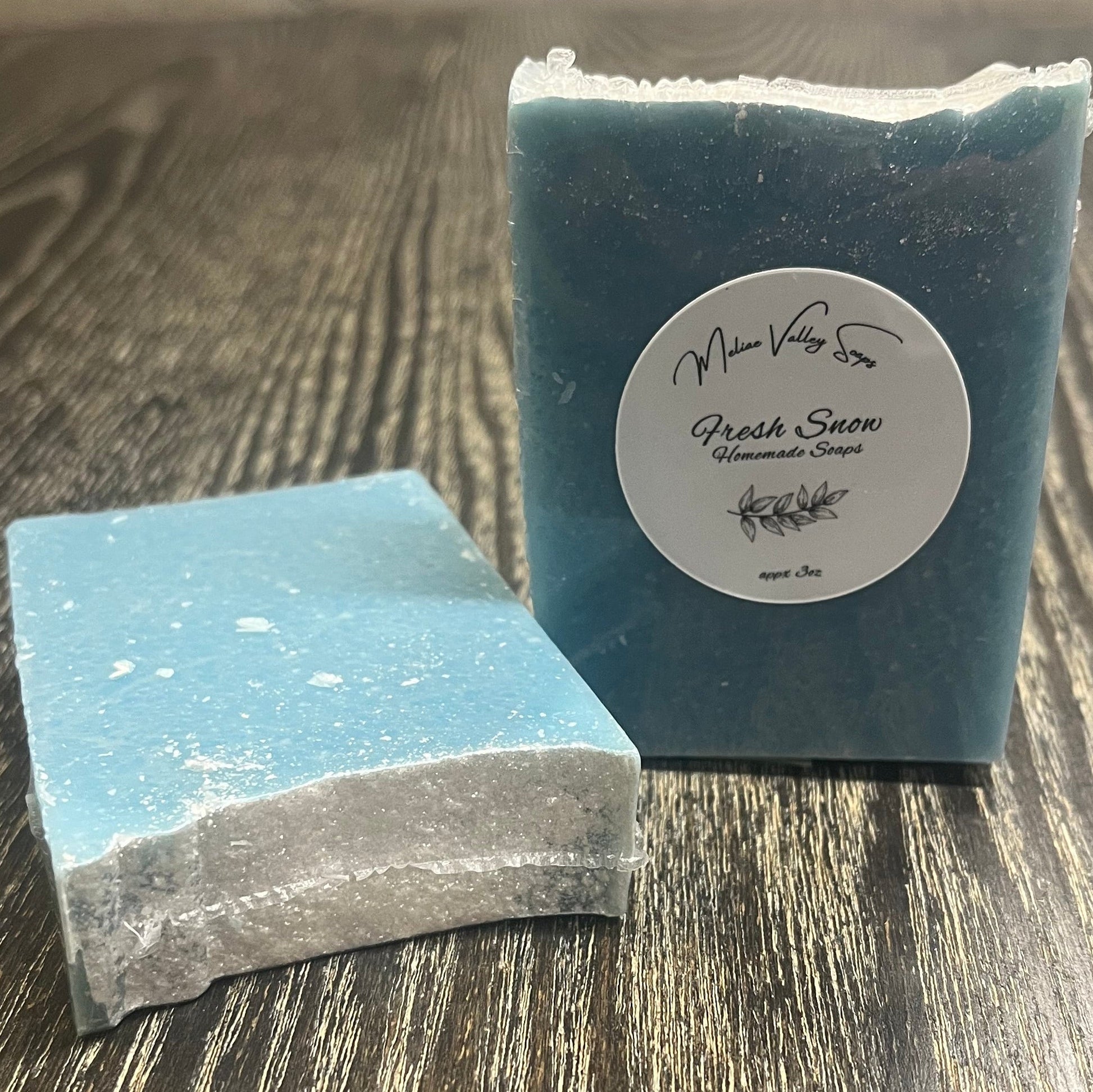 Two tall blue bars of soap with a heavy sprinkle of glitter on top. The left one is face down, showing the back and top, while the right one shows the front. 