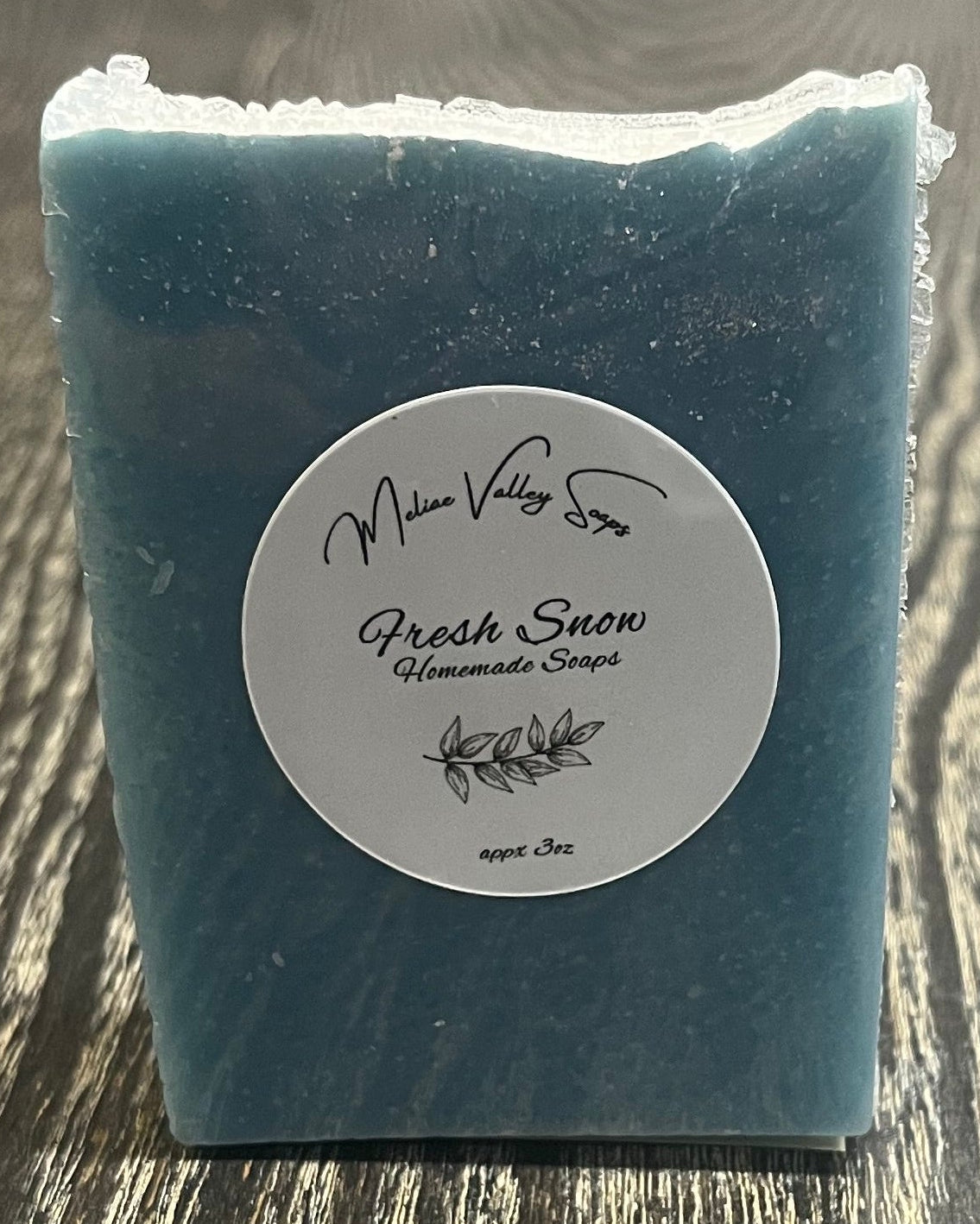 A tall blue bar of soap with a heavy sprinkle of glitter on top faces the camera, showing a white label. 
