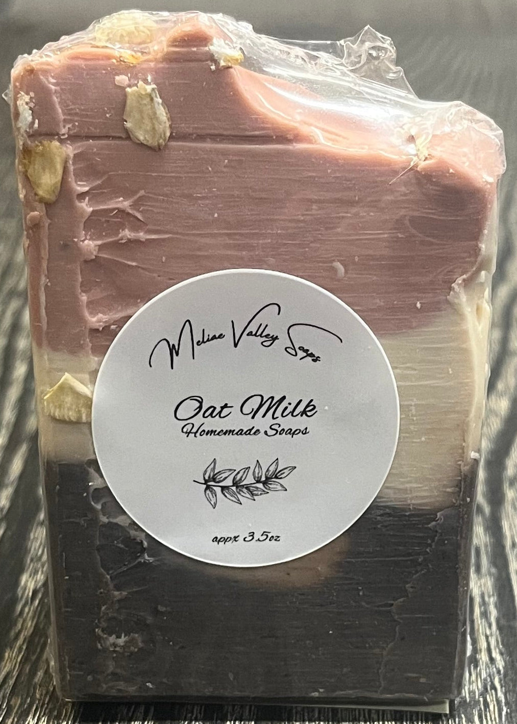 A tall soap bar with a dark brown bottom layer, a beige middle layer, and a pink top layer. The top layer is swooped to the side. The bar has a white label. 