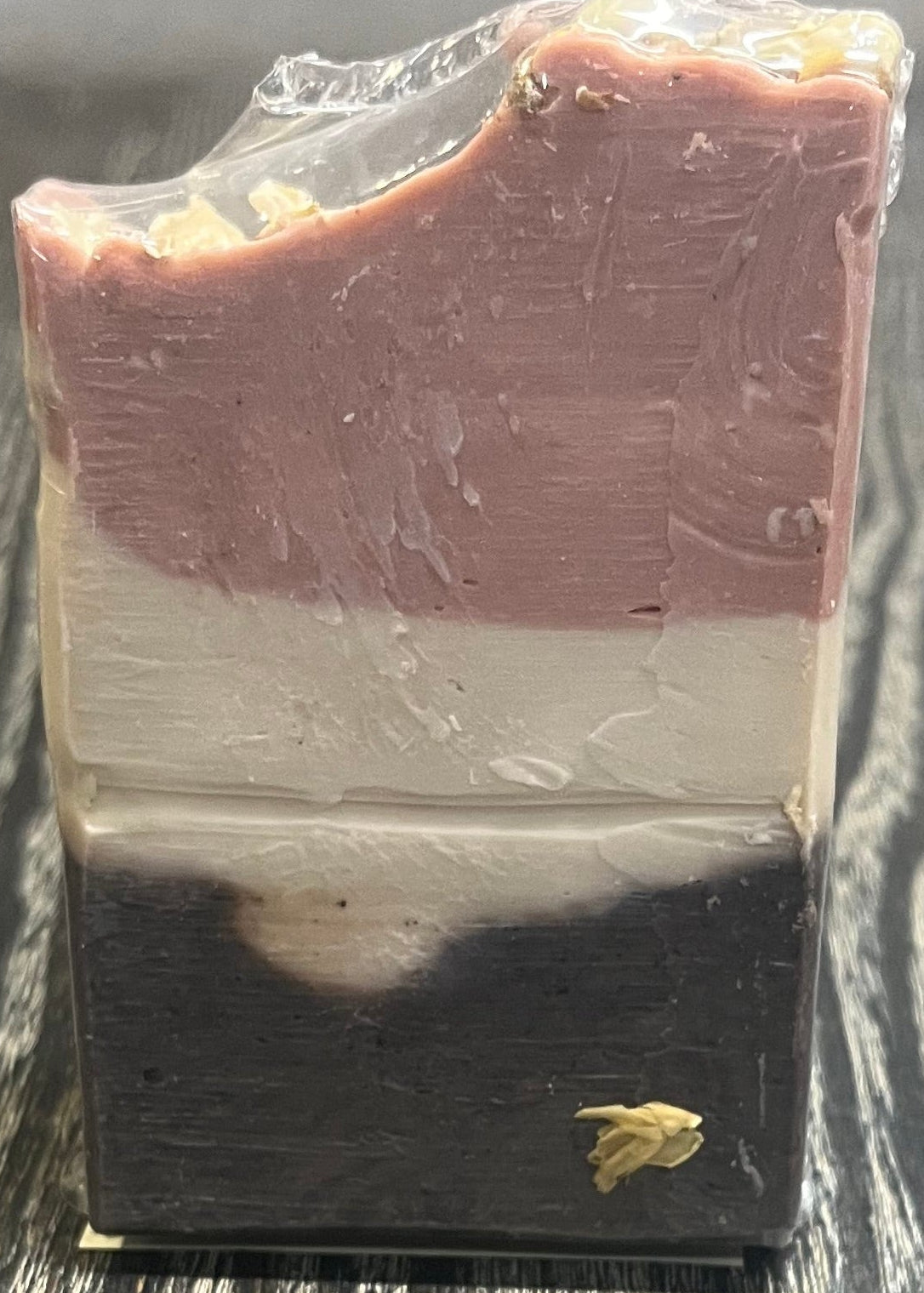 A tall soap bar with a dark brown bottom layer, a beige middle layer, and a pink top layer. The top layer is swooped to the side. 