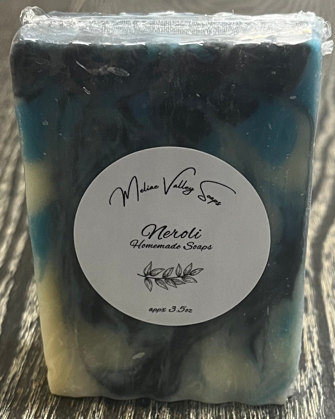 Bar of soap with navy blue, blue, and white swirl design with a white label on a wooden surface. 