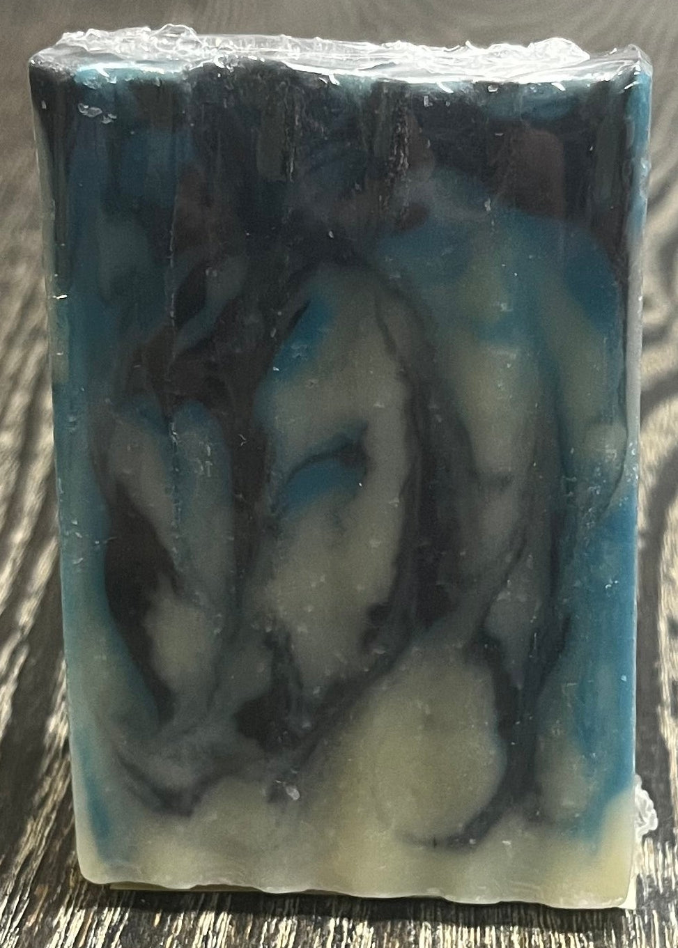 Bar of soap with navy blue, blue, and white swirl design on a wooden surface. 