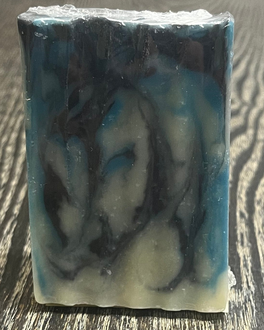 Bar of soap with navy blue, blue, and white swirl design on a wooden surface. 